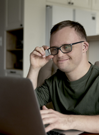 Man with Down syndrome smiling while using a laptop at home