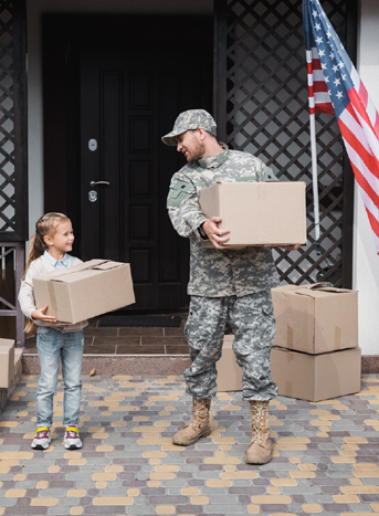 U.S. military service member and young daughter carrying moving boxes outside a home